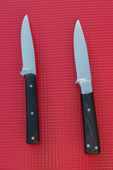 A pair of paring knives on a red background