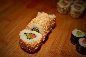 Sliced Japanese sushi roll maki with rice, salmon, avocado and cucumber covered with sesame seeds on wooden table