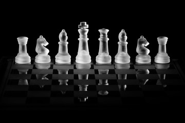 Glass Chess Set Standing on a Chessboard with a Dark Background, including the Rook, Knight, Bishop, Queen and King Pieces