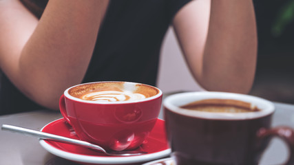 Closeup image of a latte coffee cup and Americano coffee with woman sitting in cafe background