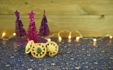 Christmas food photography picture of traditional mince pies and glitter tree decorations with fairy lights and blue gold star table cloth with wood background