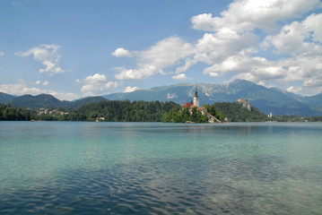 Turquise Lake Bled with Church of the Assumption in front of Bled Castle and mountain range