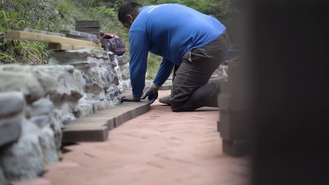 Man lining up bricks for the soldier course along a rock wall as part of a hardscaping patio project.