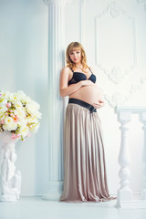 beautiful pregnant girl in a pink skirt with a naked belly with white flowers