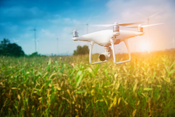 Drone flying above the corn field for survey the crop and wind turbine background