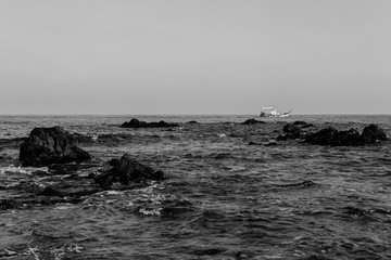 Rocky seashore and passing boat in Pomos, Cyprus in monochrome