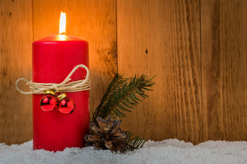 Lit Christmas Candle with Pine Branches, a Cone and Snow on a Wooden Background