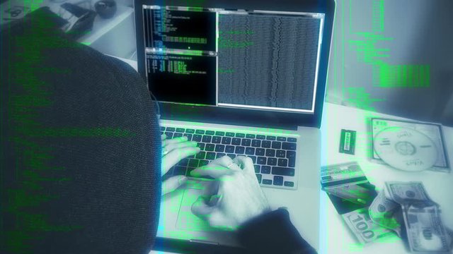 Hooded Hacker Working On Laptop, Slow Zoom. Hooded person typing in a laptop next to stolen itens, simulating a hacker crime scene