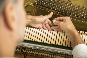 Technician tuning a upright piano using lever and tools