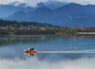 Fototapeta na wymiar Serenity morning on Alpine lake with red boat and foggy mountains