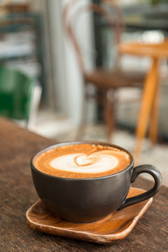 Hot latte coffee with latte art in a matt black cup on the wooden table in a coffee shop background