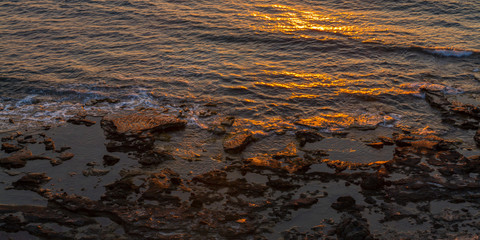 Rocky seashore and sun reflections at sunset in Pomos, Cyprus