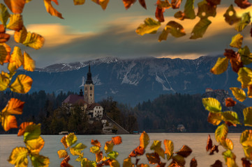 Bled, Slovenia - Beautiful autumn sunset at Lake Bled with the famous Pilgrimage Church of the Assumption of Maria with Bled Castle and Alps at background. Moving clouds  framed with autumn foliage