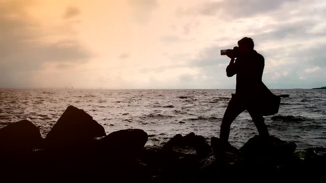 Silhouette of photographer on shooting a seascape. Enthusiastic creative person with a camera. To capture nature in photographs. Turbulent seas and a photographer in the wind. 