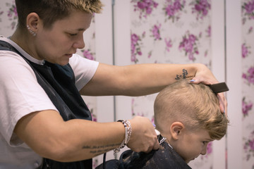 Little boy getting a haircut by female hairdresser.
