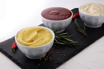 Classic set of sauces in white saucers: American yellow mustard, ketchup, mayonnaise