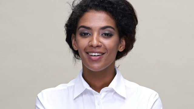 Close up view of smiling african woman in shirt sends air kiss at the camera over gray background