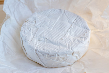 Camembert or brie cheese in white paper on wooden background
