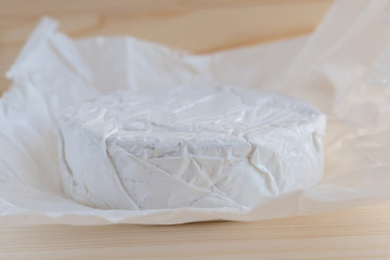 camembert cheese im white paper on wooden background closeup