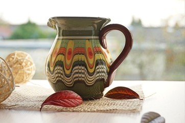A decorative small jug with patterns stands at the window. outside the window is cloudy weather, autumn.