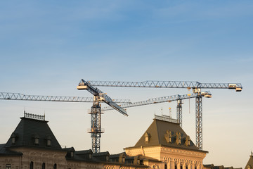 tower cranes above old roofs at construction site in morning sunlight