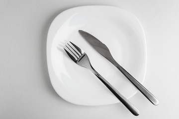 empty white plate, fork and knife on a white background.