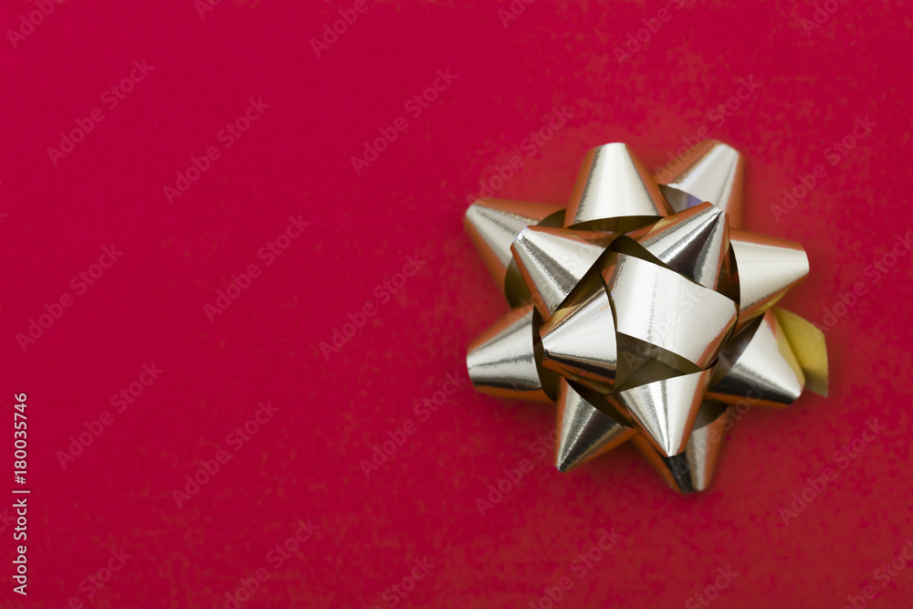 Wall mural Metallic gift bow on a red background