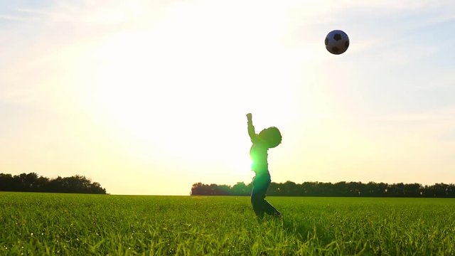 Happy child playing with a ball on the lawn against the sunset background. The boy throws the ball at a slow pace