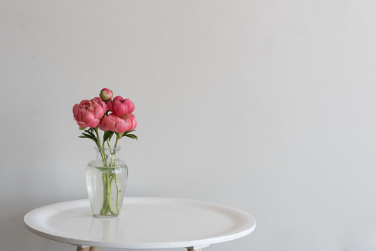 Fototapeta Small bunch of coral peonies in glass vase on round white table against neutral background with copy space