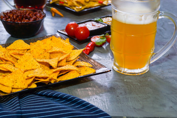Nachos  with Tortilla chips tomato salsa, bean and mustard and two glass with beer on rustic stone background.