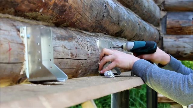 Assembling a wooden frame and building a house. Russia. The worker fixes fastenings for floor construction in a wooden house, drills screw holes with a drill tool.