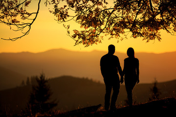 Young couple hiking outdoors with backpacks during sunset. Silhouette of a couple on the top of a rock mountain view of sunset.  activeactivityadventurealtitudeautumnbackpackbackpackingcampingcliffcli