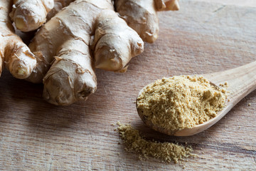 Ground ginger on a wooden spoon, with fresh ginger in the background