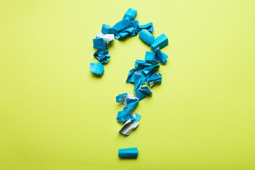 A large question mark from pieces of crumpled blue paper on a yellow background.