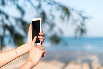 Hand of woman using smartphone mobile, blur the background of the beach.