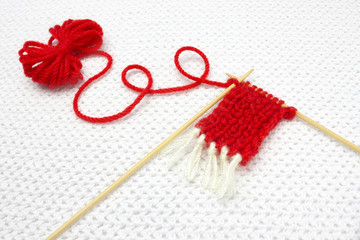 A small red yarn ball and the beginning of red Santa scarf on the white crochet background. Romantic Christmas concept. Knitting with love.