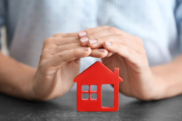 Woman holding hands over wooden figure of house at table, close up