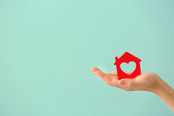 Woman holding wooden figure of house on color background