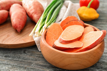 Bowl with raw sweet potato on wooden table