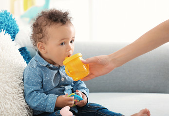Mother giving baby bottle with water indoors