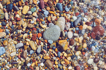Multicolored sea pebbles in the wave on the shore