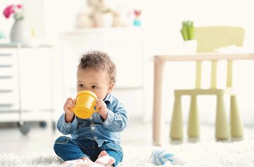 Cute baby with bottle of water on floor at home