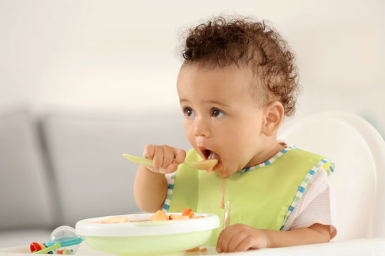 Little baby eating fruit puree indoors