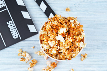 Cup with caramel popcorn and movie clapper on wooden background