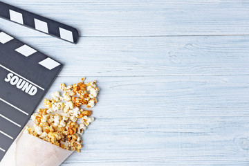 Paper cone with caramel popcorn and movie clapper on wooden background