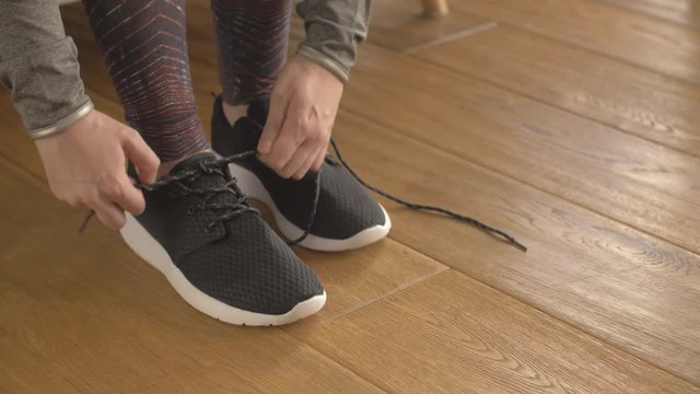 Fit Woman Tying Laces Of Sport Shoes On Hardwood Floor