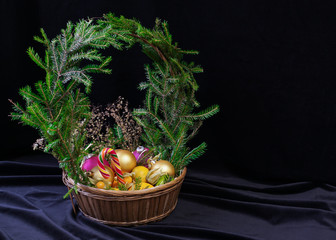 A large basket of fruit and Christmas balls. Crowned wreath of spruce branches. It is on the table.
