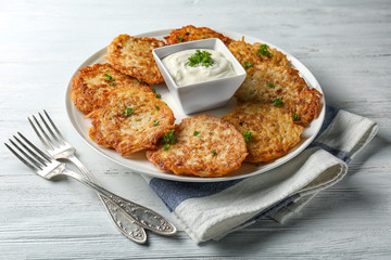 Plate with Hanukkah potato pancakes and sauce on table
