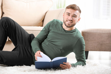 Young man reading book on floor near sofa at home