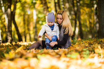 Happy family mother playing with child in autumn park near tree lying on yellow leaves. Autumn concept.